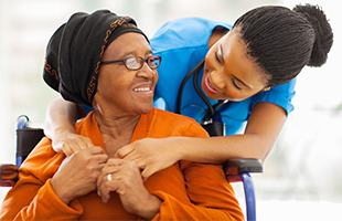 older woman with headwrap embraced from behind by younger medical professional