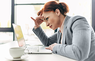 red haired woman pensively looking at laptop