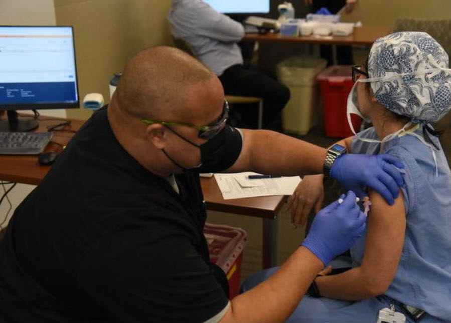 healthcare worker in mask gives COVID-19 vaccination to another healthcare worker in mask