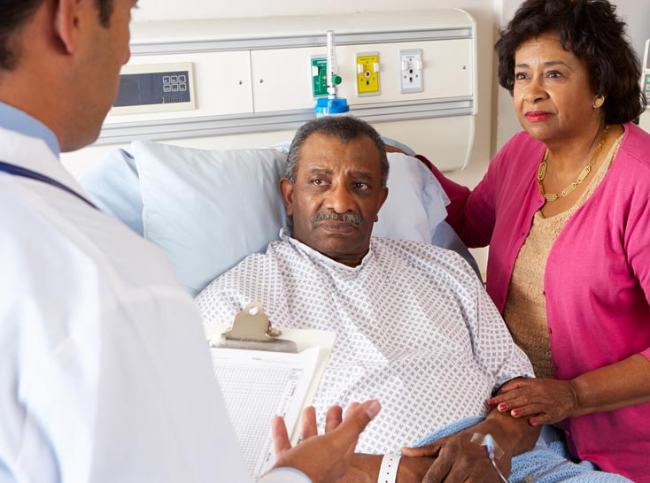 A physician talks with a patient who is sitting in a hospital bed